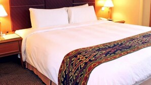 Habitación de hotel con una cama grande, dos lámparas de noche, cabecera de madera y una manta decorativa.