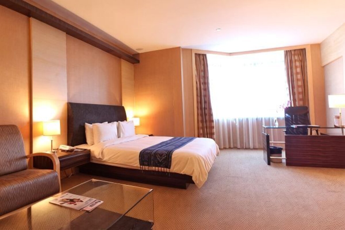 A hotel room with a bed, a desk, a chair, a coffee table, and a nightstand.
