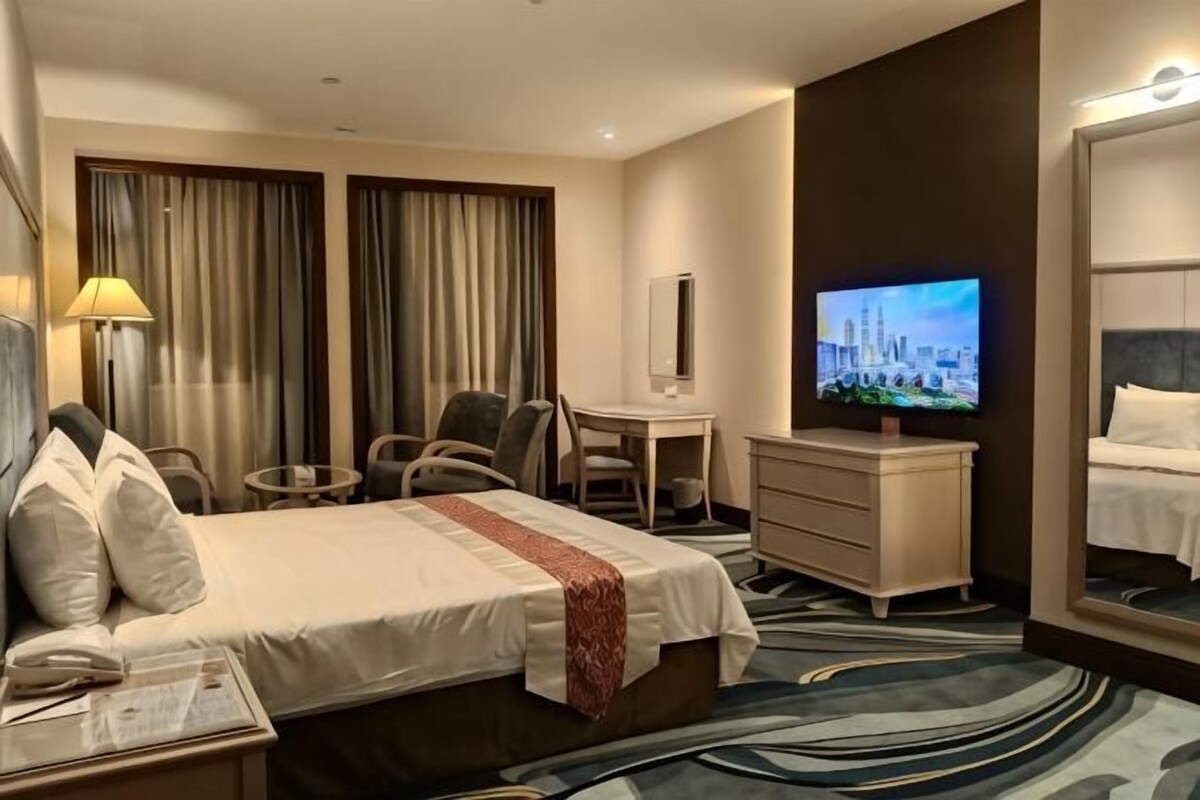 A hotel room with a bed, desk, chair, television, and a mirror.