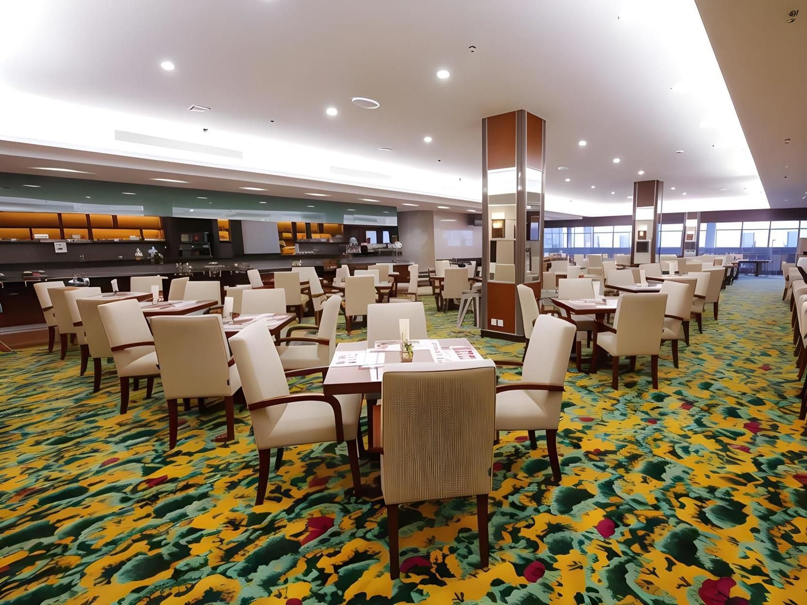 Ein Speisesaal eines Hotels mit mehreren Tischen und Stühlen, einer zentralen Säule und einem gemusterten Teppich.