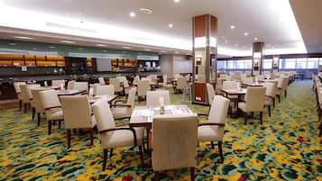 Ein Speisesaal eines Hotels mit mehreren Tischen und Stühlen, einer zentralen Säule und einem gemusterten Teppich.