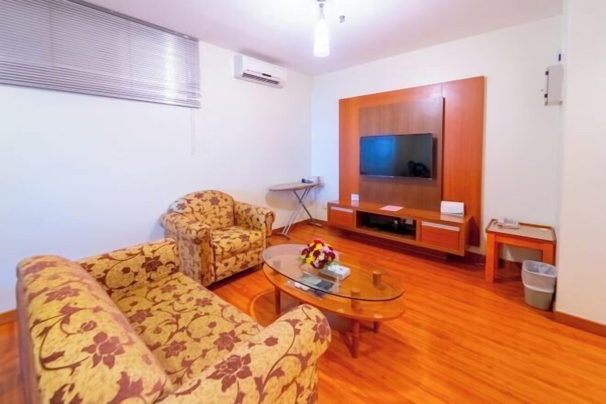 A living room with a sofa set, a coffee table, a TV, and a small table with a trash bin.