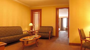 Quarto de hotel com sofá, poltronas, mesa de centro e porta que dá para outro cômodo.