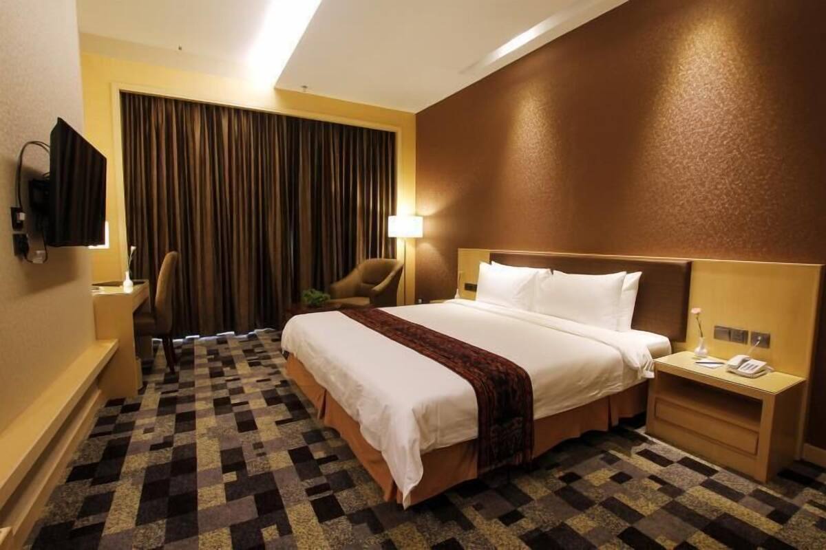 Habitación de hotel con cama, escritorio, silla, televisor y ventana con cortinas.