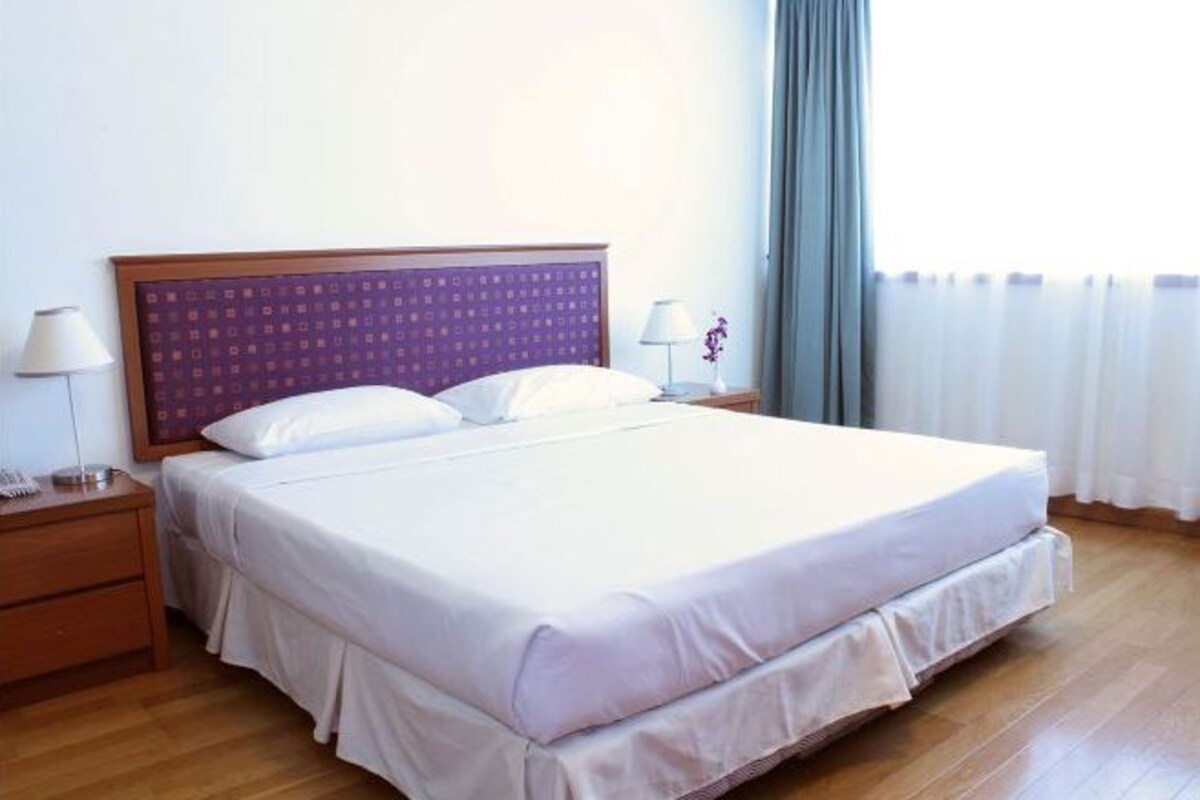 A standard hotel room with a single bed, a nightstand, a lamp, and a window with curtains.