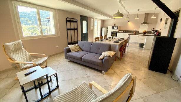A spacious living area with a sofa, chairs, a dining table set for four, and a kitchen in the background.