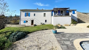 A two-story building with a white facade, blue shutters, and a stone wall.