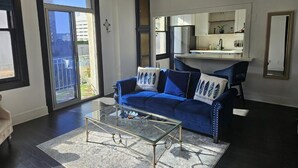A living room with a blue sofa, a glass coffee table, and a chandelier. - Luxe Suite one bedroom condo with ocean view balcony and free secure parking (Long Beach)