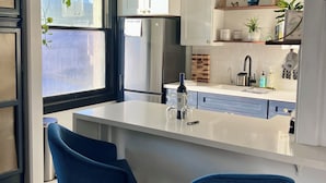 A modern kitchen with a central island, bar stools, and a window overlooking a cityscape. - Luxe Suite one bedroom condo with ocean view balcony and free secure parking (Long Beach)