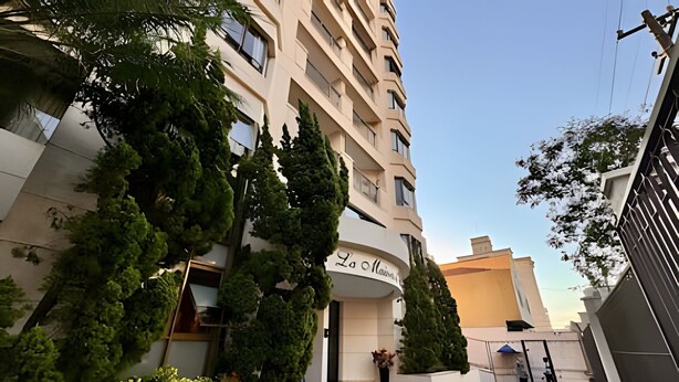 Entrada de hotel con fachada curva, un cartel que dice "La Maison" y un patio empedrado con vegetación.