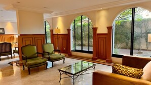 Un vestíbulo amplio con una mesa de centro de vidrio, dos sillones y un sofá. Grandes ventanas de arco ofrecen vistas a zonas verdes exteriores.