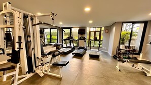 Un gimnasio con diverso equipo de ejercicio, amplias ventanas y suelo de hormigón.