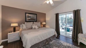 A bedroom with a large bed, two bedside tables with lamps, a ceiling fan, a window with curtains, and a view of the outdoors. - Beautiful South Facing Pool Home (Kissimmee)