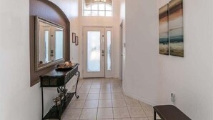 A hallway with a large mirror, a bench, a door with frosted glass panels, and a painting on the wall. - Beautiful South Facing Pool Home (Kissimmee)