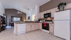 A modern kitchen with a central island, white cabinetry, a microwave, and a refrigerator. - Beautiful South Facing Pool Home (Kissimmee)