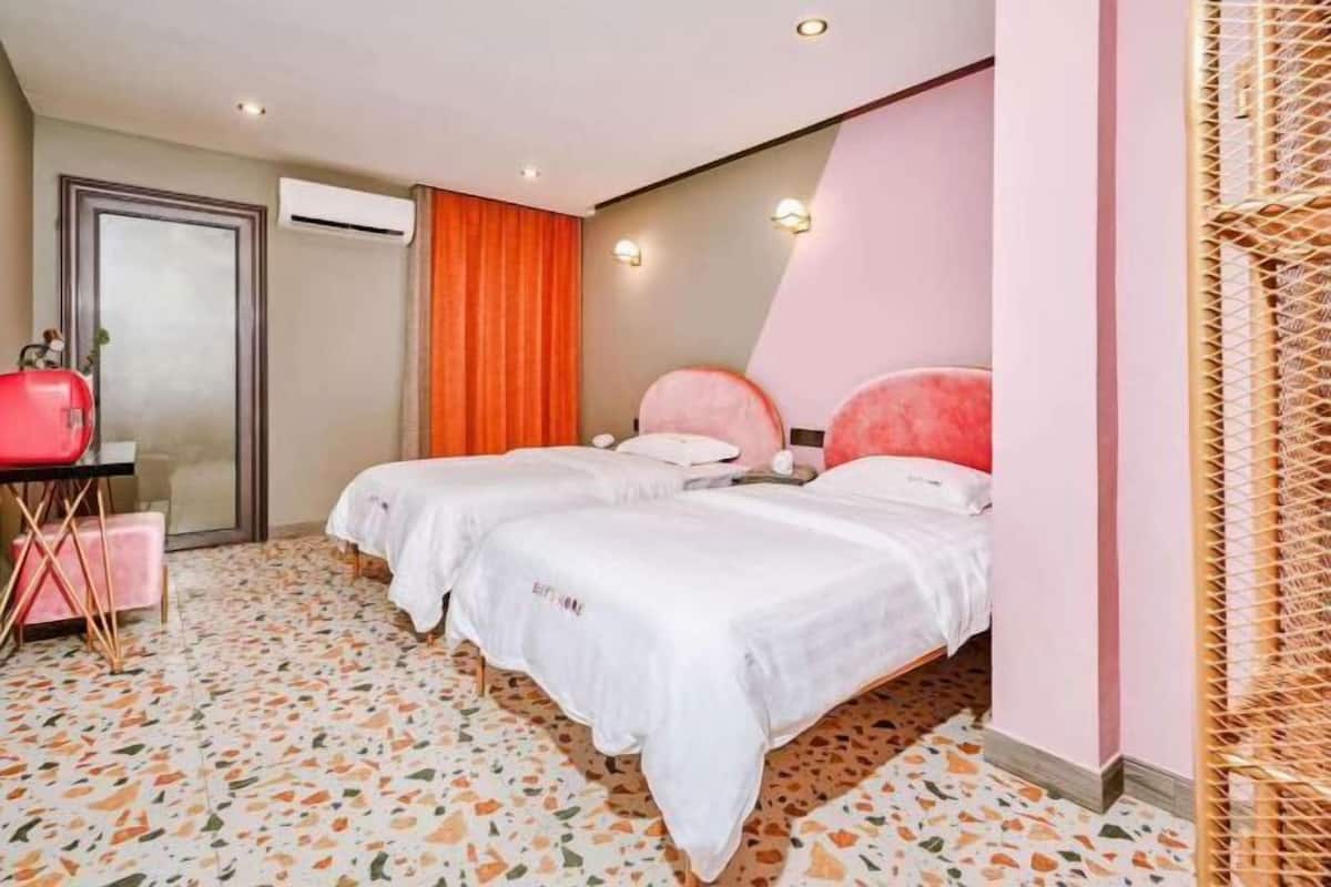 A hotel room with two beds, a small desk, and a mirror.