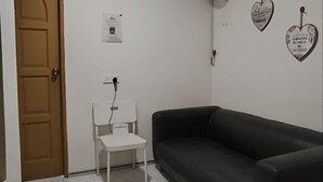 A room with a black leather sofa, a white chair, a desk with a lamp, and a wall-mounted fan. - Natol Homestay-MJC Batu Kawa MJC New Township (Kuching)