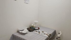 A small, clean room with a bed, a bedside table, and a chair. There is a small table with a tissue box, a cup, and a decorative item. - Natol Homestay-MJC Batu Kawa MJC New Township (Kuching)