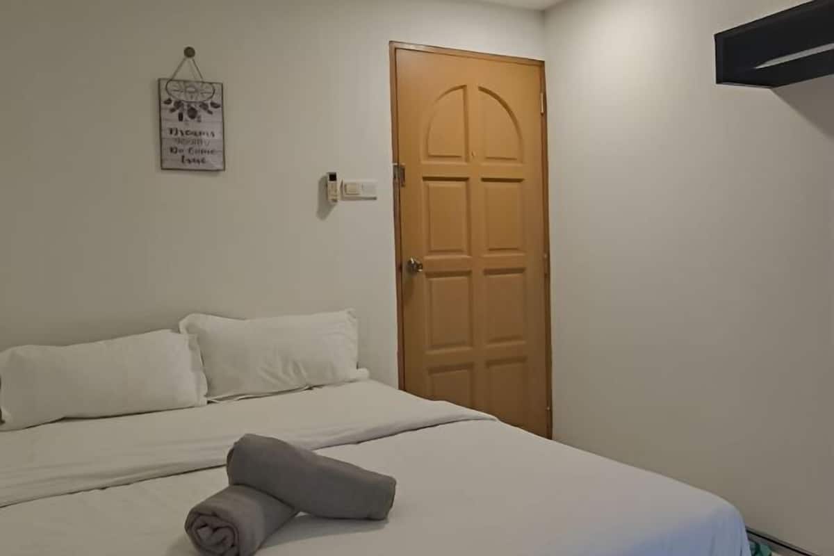 Un lit bien fait, avec du linge de lit blanc, une porte en bois et un interrupteur fixé au mur.