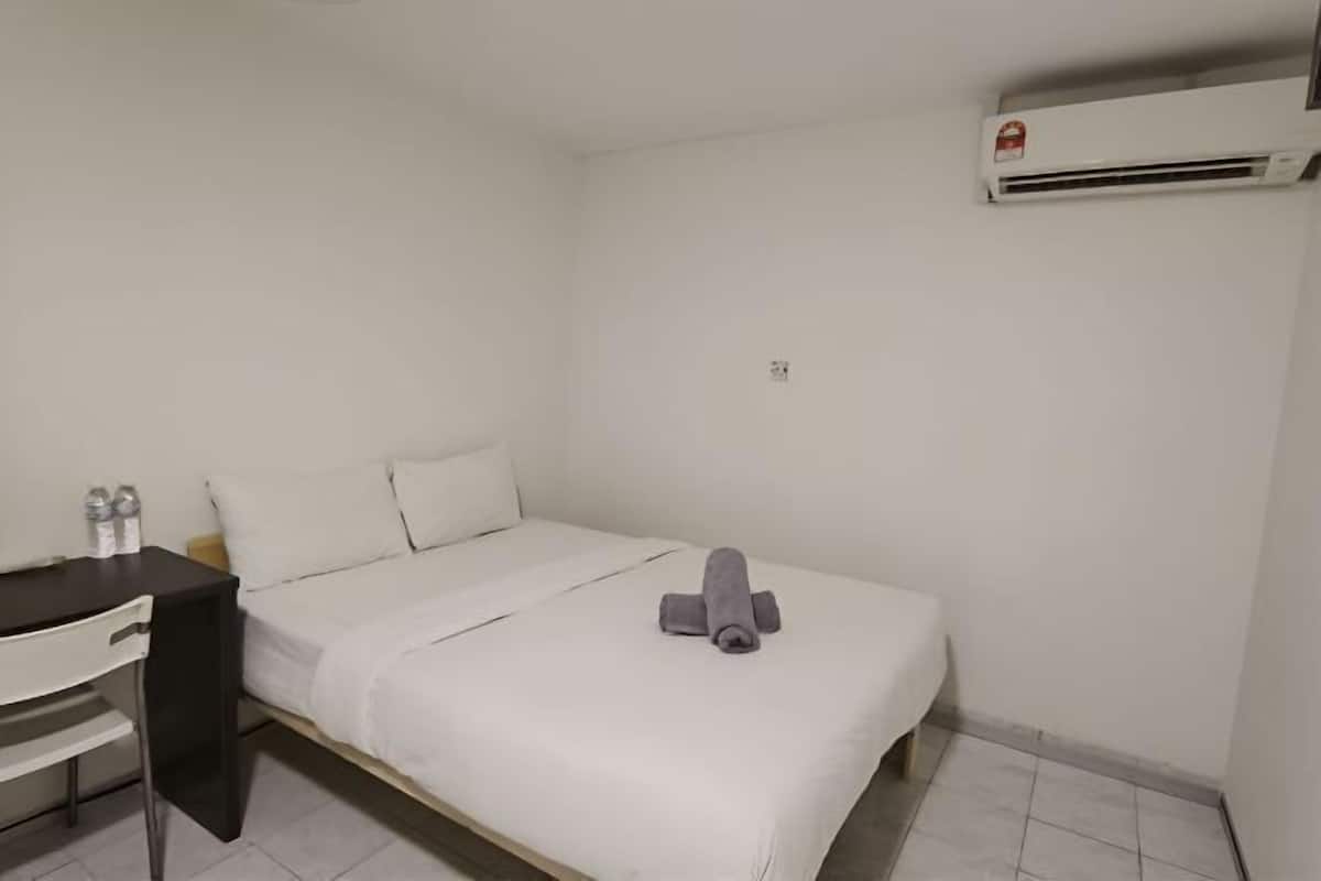 Une petite pièce propre, équipée d’un lit, d’un bureau et d’un appareil de climatisation.