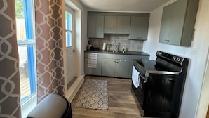 A compact kitchen with grey cabinets, a black stove, and a window with blue curtains. - Beautiful Downtown Core Apt. Located on Main Street, Kentville (Kentville)
