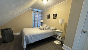 A bedroom with a bed, a bedside table with a lamp, a suitcase, and a wall with motivational posters. - Beautiful Downtown Core Apt. Located on Main Street, Kentville (Kentville)