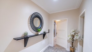 A hallway with a black wall-mounted shelf holding a mirror and a small plant, leading to a door. - Villa Magnum (Douala)