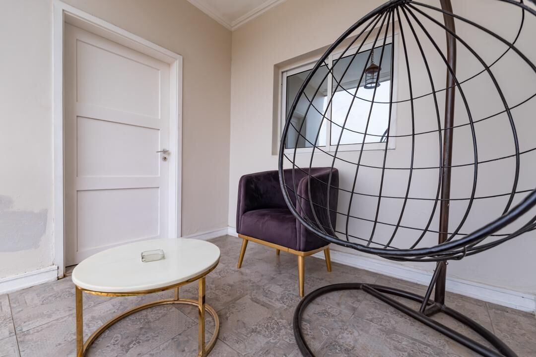A room with a white door, a round table with a gold frame, a purple chair, and a black wire chair.