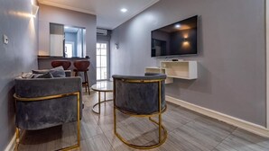 A modern living room with a grey sofa, two bar stools, a flat-screen TV mounted on the wall, and a wooden floor. - Villa Magnum (Douala)