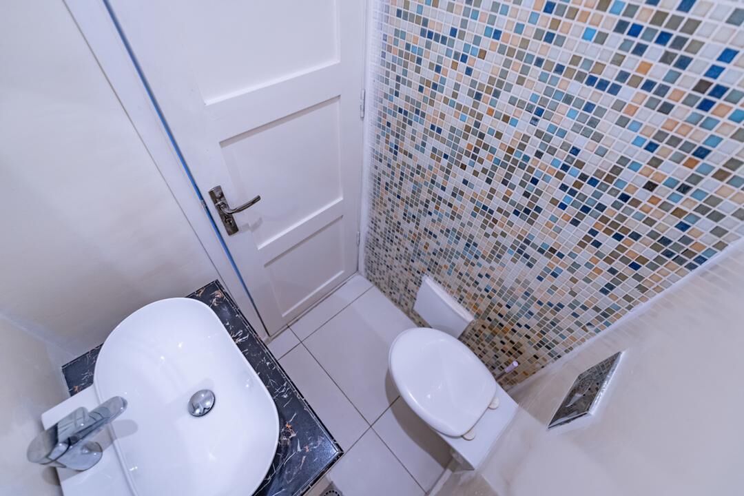 Un baño con lavamanos blanco, inodoro y paredes con azulejos.