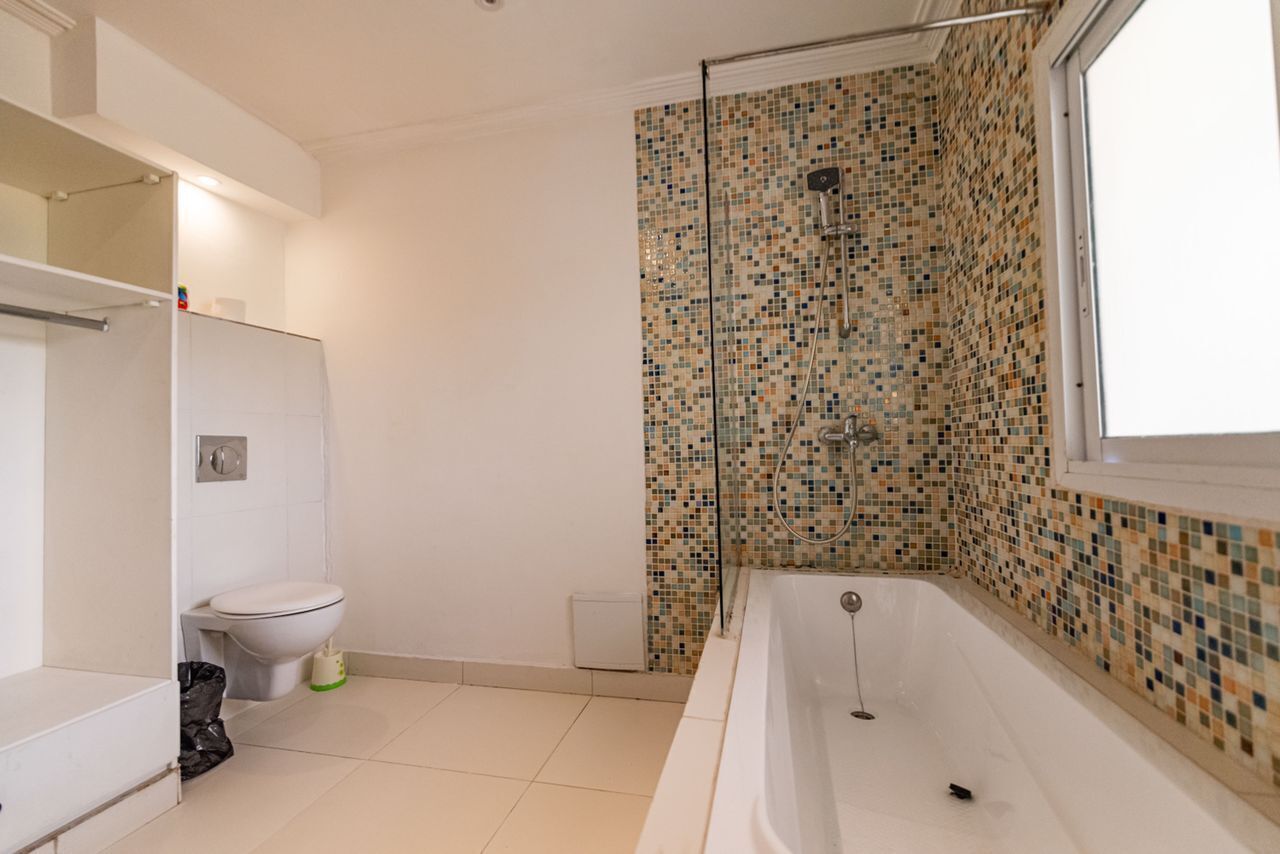 A bathroom with a mosaic shower wall, a bathtub, and a toilet.