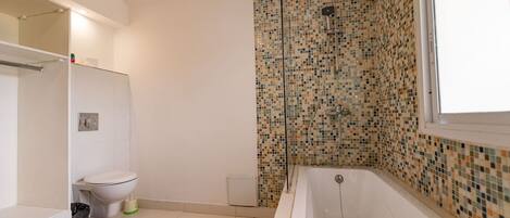 Un bagno con parete doccia in mosaico, una vasca e un water.