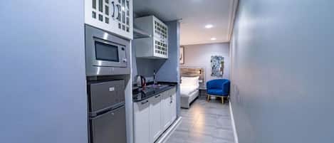 A compact kitchen with modern appliances, a small dining area, and a bed in the background.