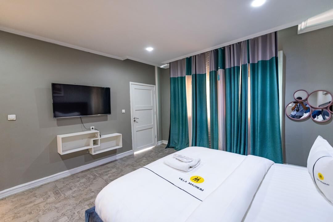 Una habitación de hotel con una cama, televisión, puerta y cortinas.