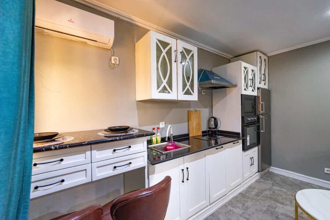 A compact kitchen with white cabinets, a black countertop, and a stainless steel range hood.