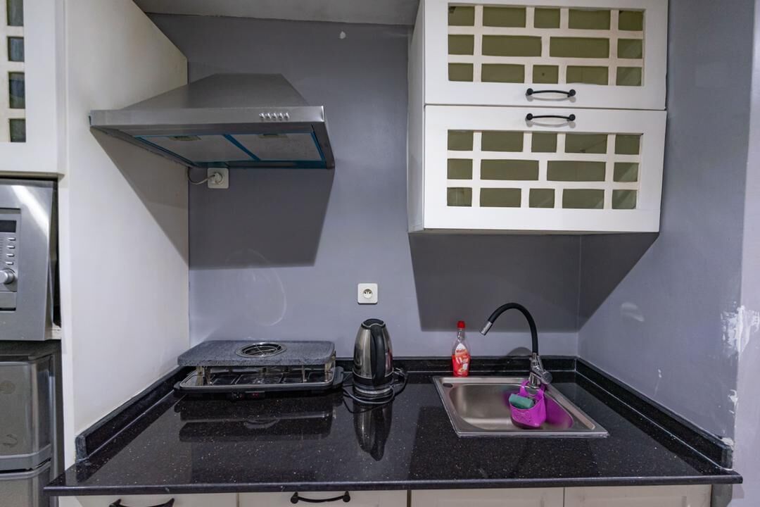 A compact kitchen with a gas stove, kettle, and a sink with a faucet.