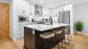 A modern kitchen with white cabinets, stainless steel appliances, a central island with stools, and a wooden door. - Canmore Spring Creek Retreat/No Sunday Scaries (Canmore)