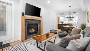 A modern living room with a fireplace, a flat-screen TV, and a dining area in the background. - Canmore Spring Creek Retreat/No Sunday Scaries (Canmore)