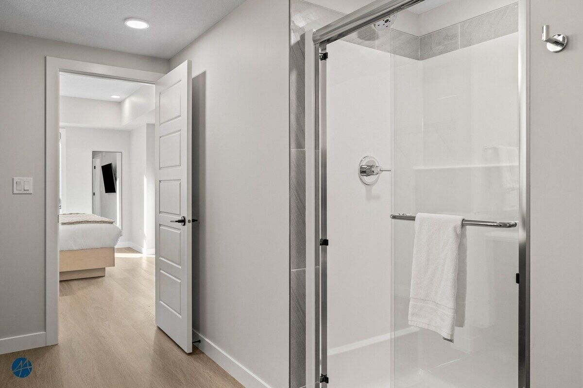 A modern bathroom with a glass shower enclosure, a visible towel rack, and a door leading to a bedroom.