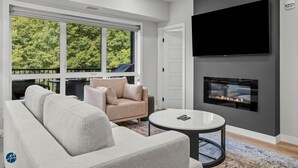 A modern living room with a large sofa, a coffee table, a fireplace, and a TV mounted on the wall.
