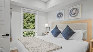 A bedroom with a large bed, a window with a view of greenery, and two wall art pieces.