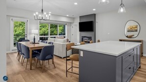 A modern kitchen with a central island, dining area with chairs, a sofa, and a fireplace.
