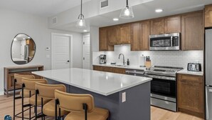 A modern kitchen with a central island, wooden cabinets, stainless steel appliances, and pendant lighting.