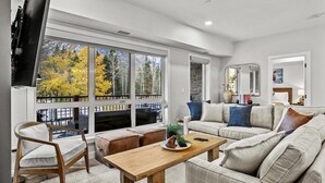 A modern living room with a large window, a sofa set, a wooden coffee table, and a television.
