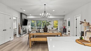 A spacious living room with a large wooden table, a chandelier, and a sofa set.