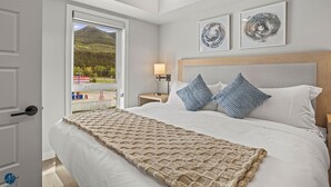 Quarto com uma cama grande, duas almofadas, mesa de cabeceira, abajur e quadros nas paredes.