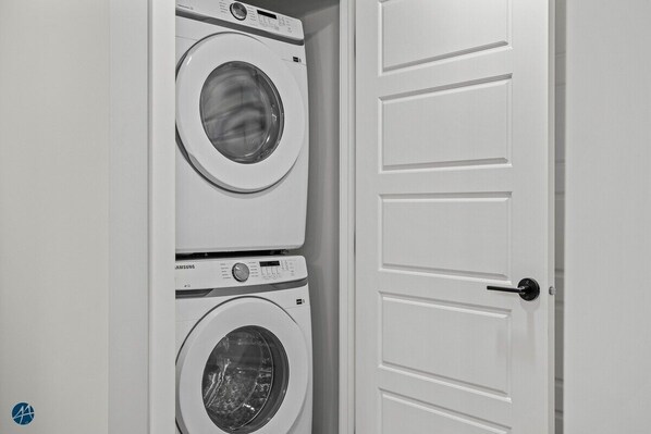 A laundry room with two stacked front-loading washing machines and a white door with a black handle.
