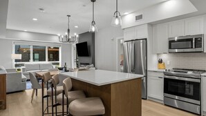 Une cuisine moderne dotée d’un îlot central, d’appareils électroménagers en acier inoxydable et d’un coin repas avec des tabourets de bar.