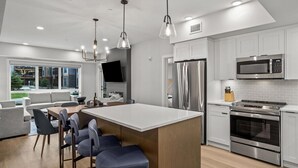 Une cuisine moderne dotée d’appareils électroménagers en acier inoxydable, d’un grand îlot central avec des tabourets, et d’un coin repas comprenant un canapé et des chaises.
