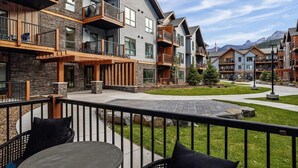 Un immeuble moderne à plusieurs étages, doté de balcons, d’un espace extérieur aménagé et offrant une vue sur les montagnes.
